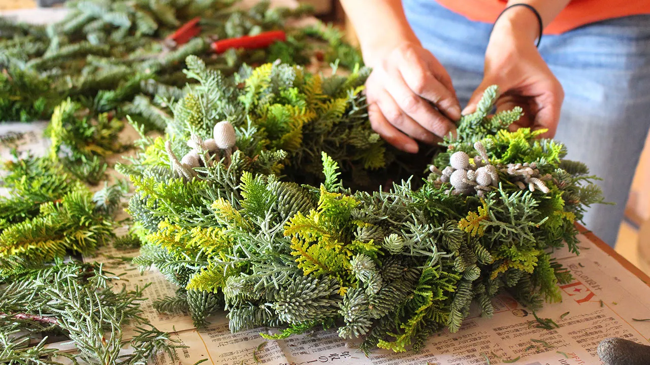 緑の葉と白い実を使って、リースを丁寧に作る手元