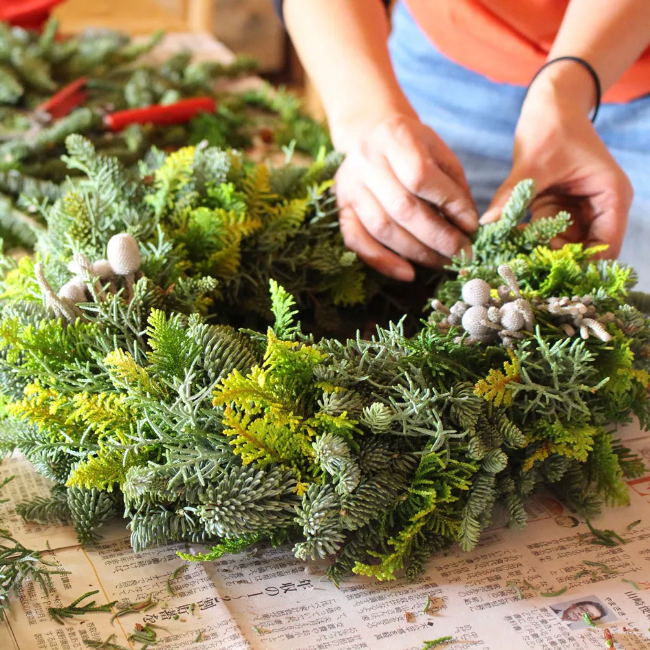 緑の葉と白い実を使って、リースを丁寧に作る手元