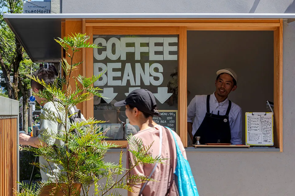スペシャルティコーヒー専門店「1983COFFEE」の木枠窓口でバリスタが接客する明るいコーヒースタンド外観