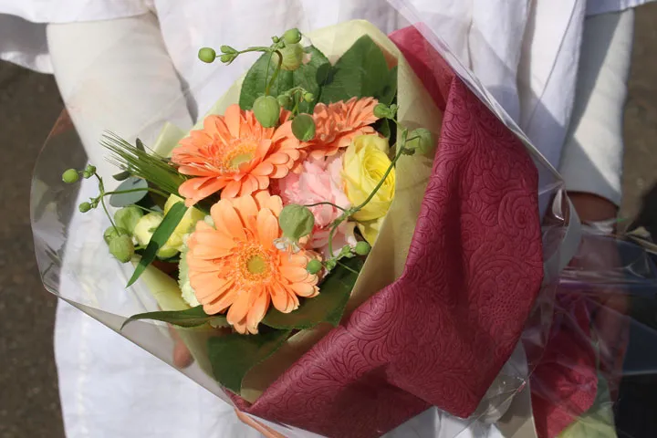 ベージュのリボンで壁にかけられた、黄色い小花と緑の葉のリース。